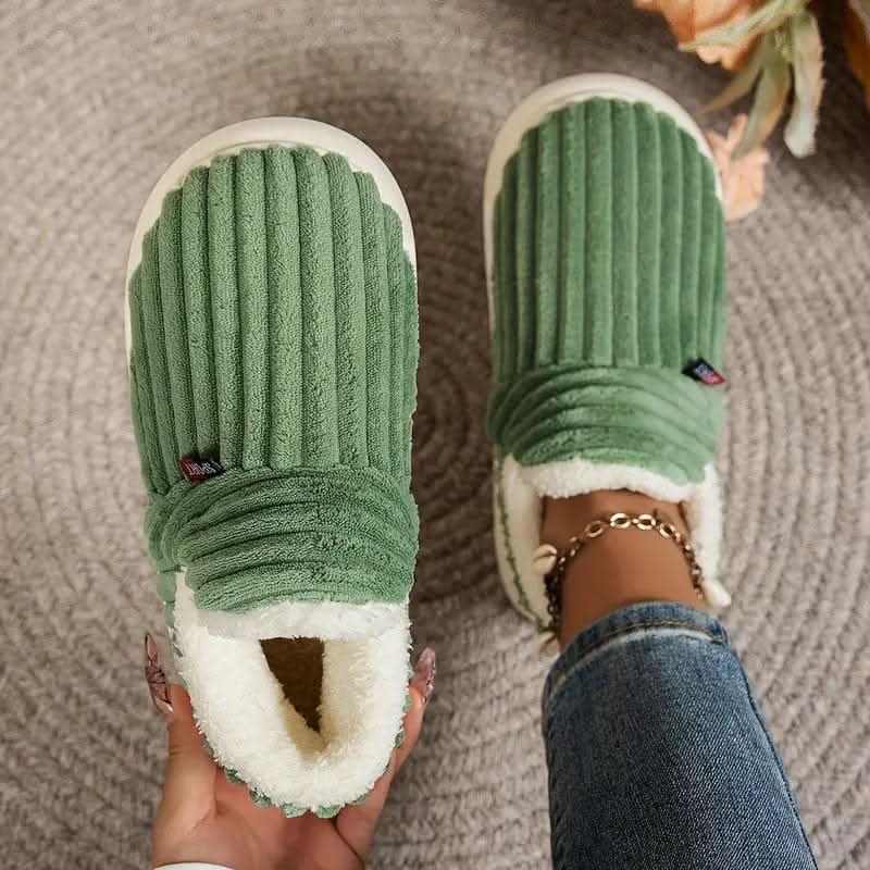 Par grå termo-hjemmesko med blødt plysfoer stillet på et trægulv